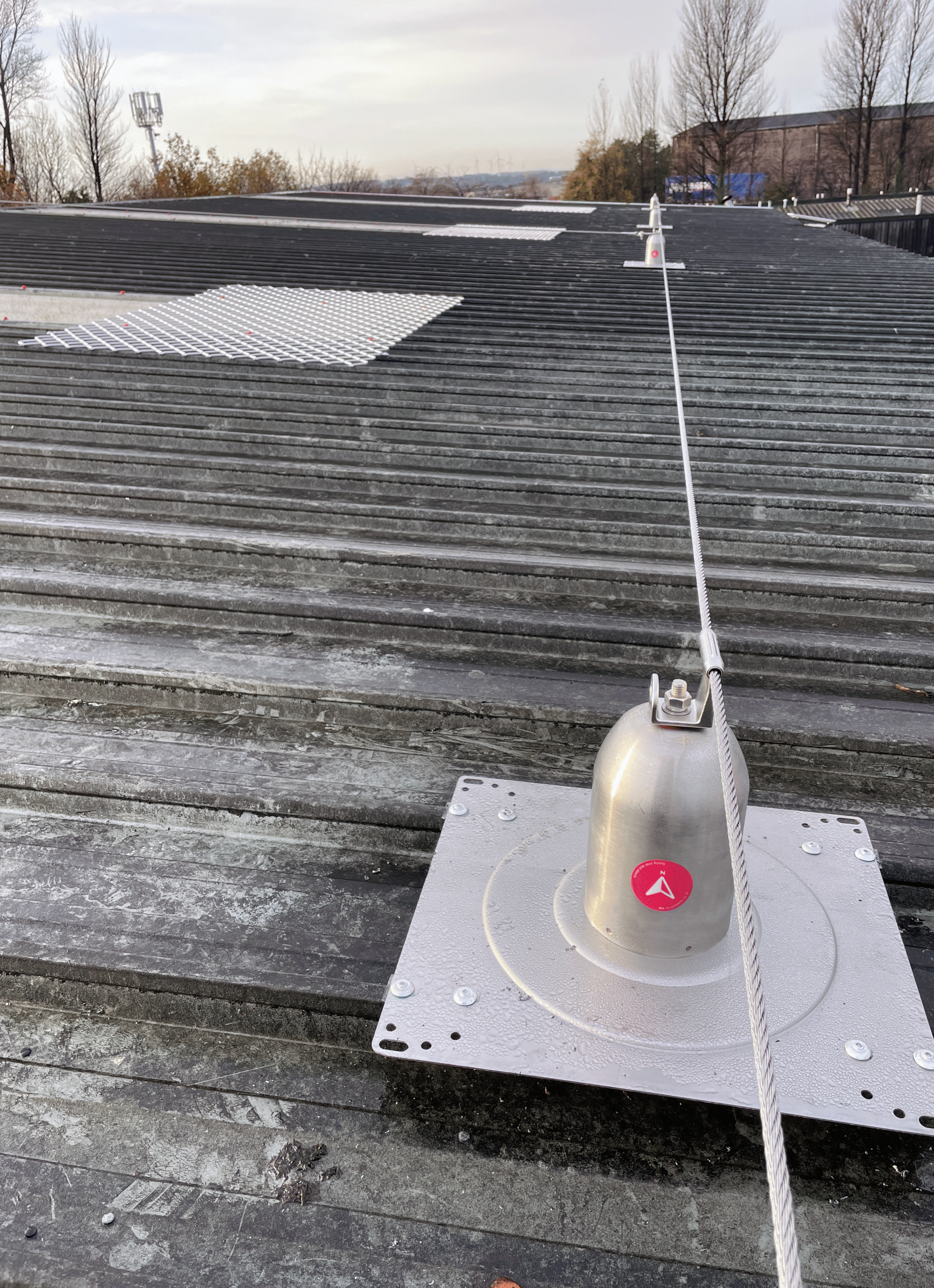 A corrugated warehouse roof with a well maintained horizontal safetyline installed. The safetyline has an Access North asset tag displayed on it.